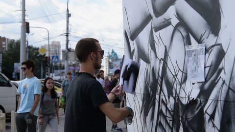 NOVOSIBIRSK, RUSSIA - AUGUST 14, 2015: Graffiti art exhibition in the city. Passers-by watching at artists drawing with sprayers in the street