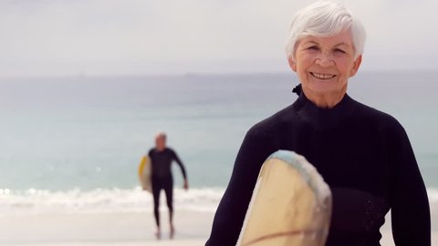 Retired couple holding surfboards on the beach