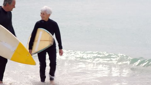 Retired couple walking with surfboards on the beach
