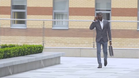 Full length portrait of a happy young man walking and talking on mobile phone, slow motion
