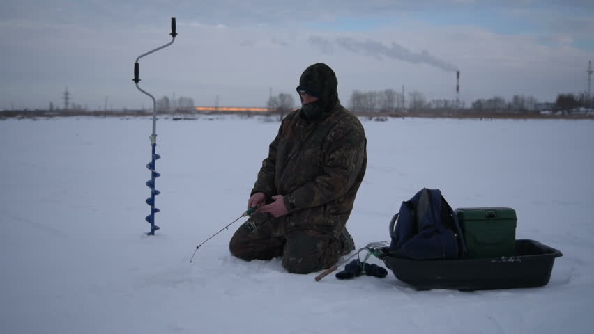 Fishing on ice. Winter. Fisherman catches a fish on a background of the urban landscape