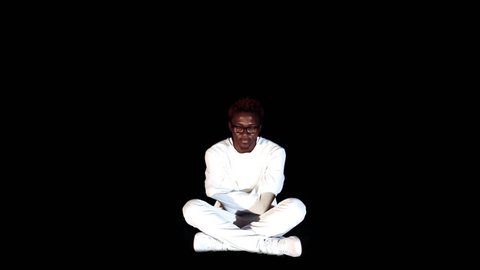An insane black man in his forties wearing a straitjacket sitting in a dark of an asylum