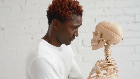 An insane black man wearing a straitjacket dance and looking at human skeleton stand