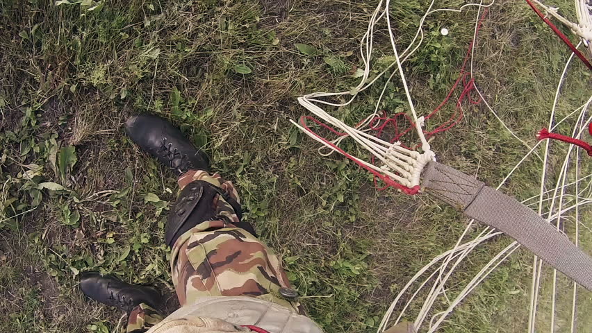Paratrooper with rifle folding parachute after successful landing on meadow