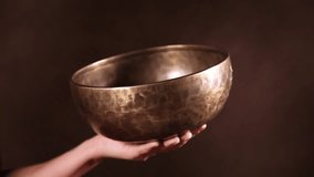 Tibetan singing bowl being made to sing in one's hand in front of brown background. Audio included
