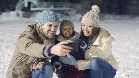 Joyous young family of three taking some happy selfies at outdoor skating rink in falling snow  : vidéo de stock