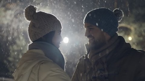 Happy couple laughing and kissing in the street light at snowy winter night 