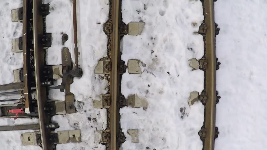 Very low altitude smooth aerial shot of railroad tracks and switches under snow