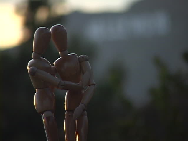 Entwined mannequins stand in front of the Hollywood sign.