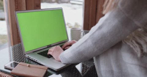 Over the shoulder shot of a woman typing on a laptop with a key-green screen. Slow Motion 4K, DCi. Woman working on computer in cozy light room at home. Surfing internet, using social network app.  