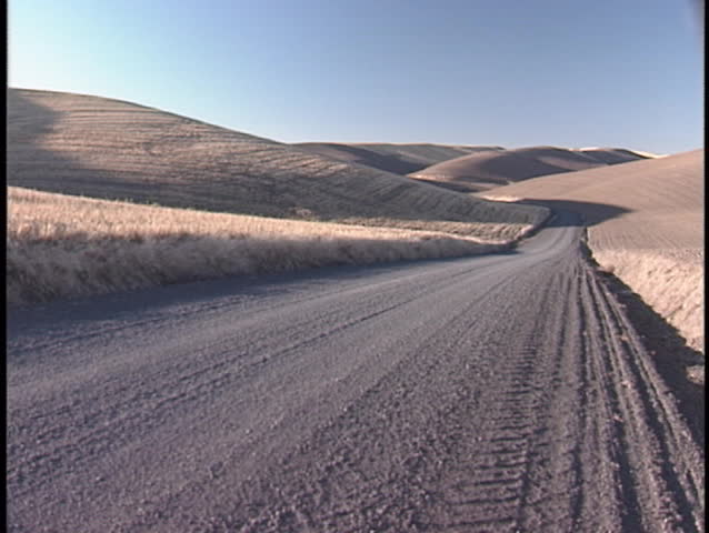 A lonely dirt road follows rolling hills into the horizon.