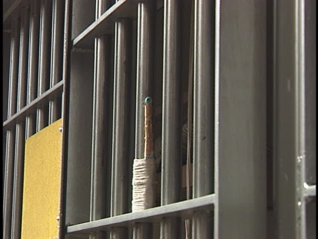A prisoner places a letter between the bars on his prison-cell.