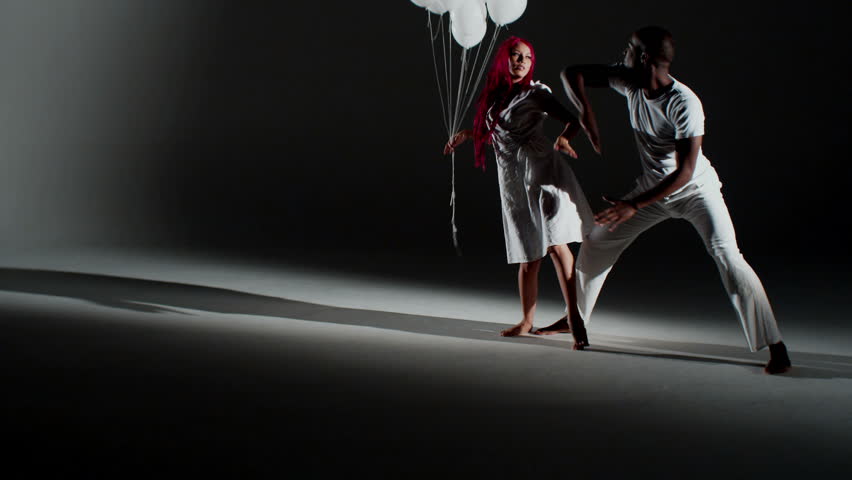An African man and Caucasian woman perform a seductive dance with balloons.