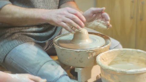 Teacher Shows the Right Position of a Hands while Molding a Clay, female hands, Male Feet in a Sneakers Are Rotating a Wheel, Man is Molding a Clay Pot, Working on a Pottery Wheel, Female Teacher,