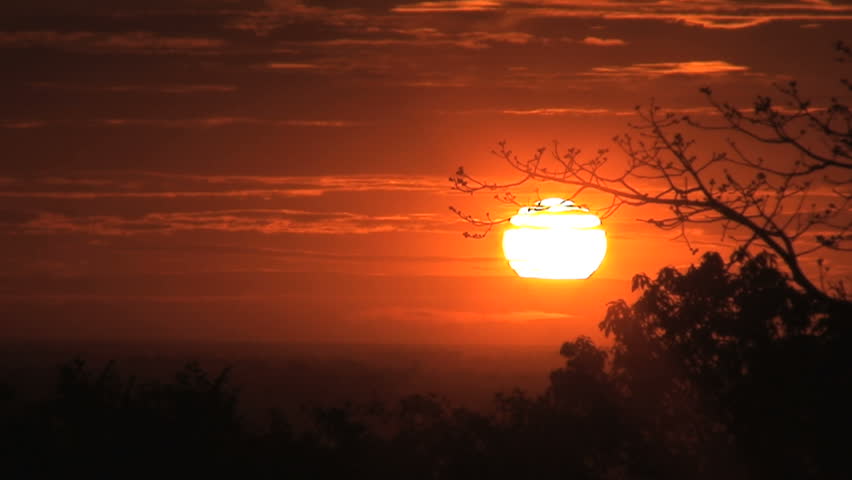 Sun setting behing clouds and trees