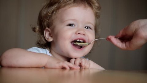 Cute little baby feeding with a spoon at the table, boy eating solid foods