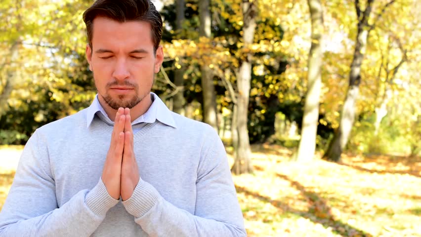 Young man stands in the woods and whith closed eyes prays.