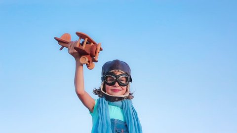Happy child playing with toy airplane against summer sky background. Slow motion