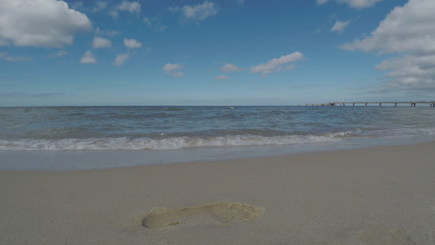 Footprint On Beach Sand Washed Away By Sea Wave. Sunny Summer Day With White Clouds And Blue Sky