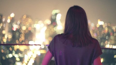 Young woman walking on terrace and admire city view during night
