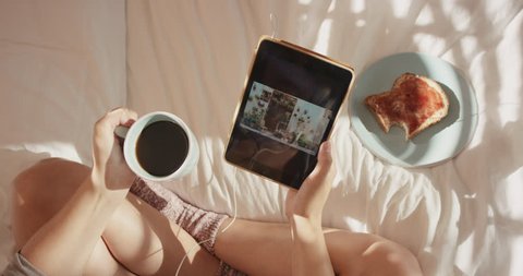 Beautiful blonde woman at home using digital tablet technology to connect drinking coffee in bed