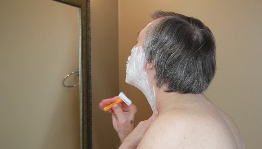 Man shaving his face while looking in the mirror with a hand razor | Shutterstock HD Video #14409379