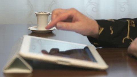 Woman works over documents using a digital tablet and drinks coffee