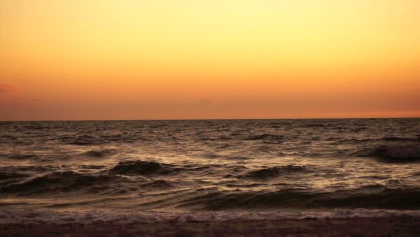 Top is an orange yellow sky of sunset and the bottom is looking directly onto crashing waves hitting the beach in the gulf of Mexico. Sunset over Bonita Beach. The waves are dark and moody.