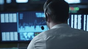 Stockbroker is talking on a headset while working on a computer in a dark office filled with display screens. Shot on RED Cinema Camera in 4K (UHD). - Powered by Shutterstock - Get 15% off with code: PIKWIZARD15