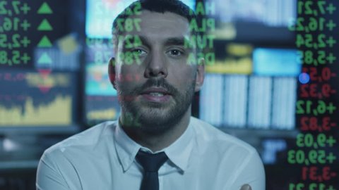 Stockbroker is looking at data with numbers on a transparent glass screen in a dark office filled with displays. Shot on RED Cinema Camera in 4K (UHD).