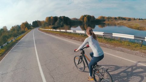 Lady cycling on the asphalt road by the autumn lake