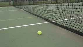 Yellow tennis ball and net on a green court.