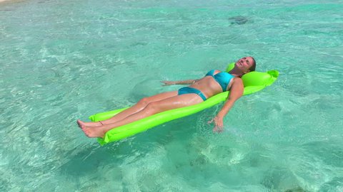CLOSEUP: Smiling young woman in bikini enjoying and relaxing on inflatable water airbed mattress floating on crystal clear ocean water surface in tropical island