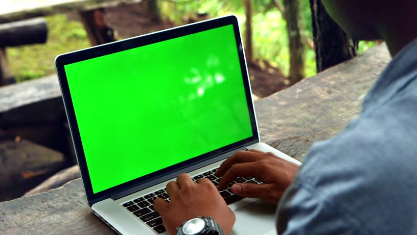 man typing on a laptop computer with a key green screen.