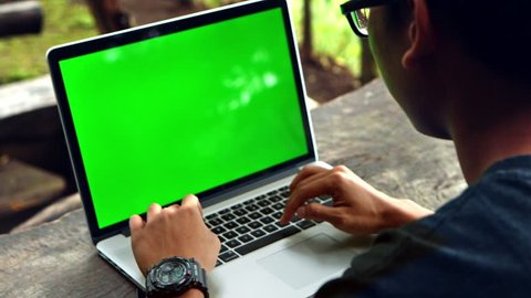 man typing on a laptop computer with a key green screen.
