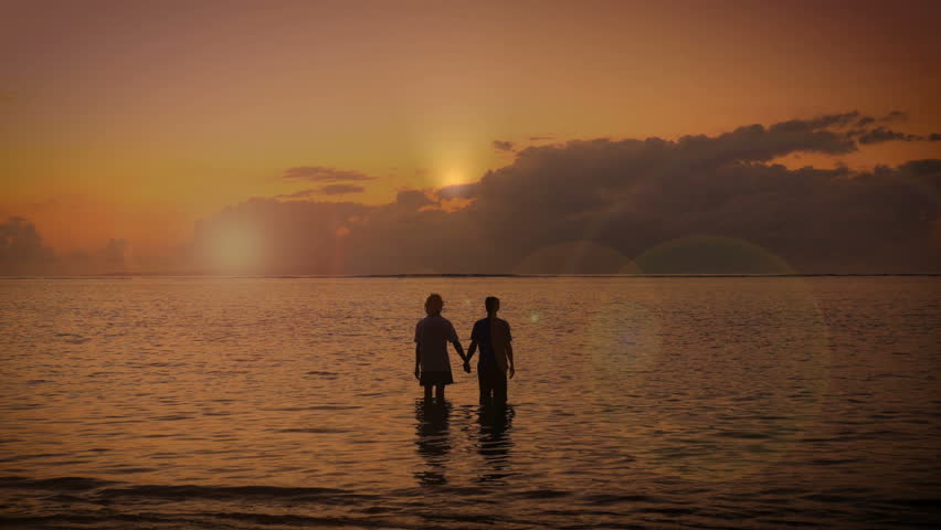 Silhouette of two adult people hold hands together and raise their arms to the sky in the Ocean as the sun rises surrendering to the good grace of the lord. Royalty-Free Stock Footage #14473774