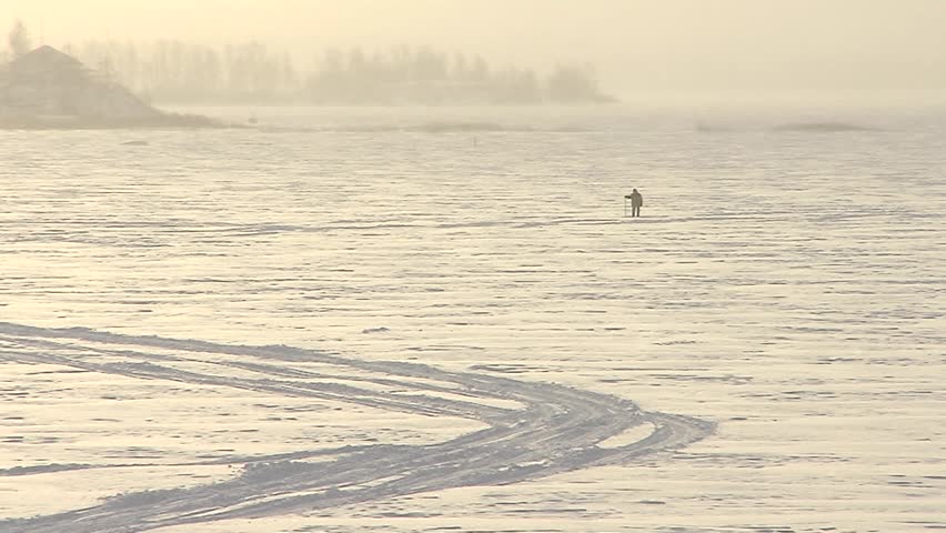 Frozen lake. A man is walking through the snow, leaning on a stick. Snowing.