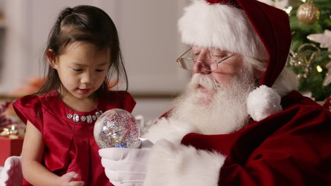 Santa Claus shows little girl a snow globe Stock Video