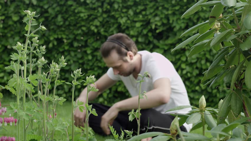 young caucasian european man with long hair stretched before or after his garden meditation. Shot on RED Scarlet 4K