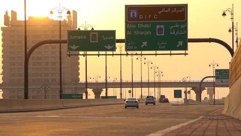 DUBAI, UAE - JULY 06, 2013: Financial Centre road at sunset, very small traffic, several cars drive along viaduct. Road navigation sign above driveway, one building and bright low sun disk
