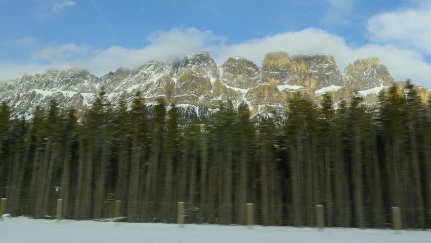 Driving past conifers with snow covered Castle Mountain in the background. Castle Mountain is located in Banff National Park in the Canadian Rockies, about half-way between Banff and Lake Louise.
