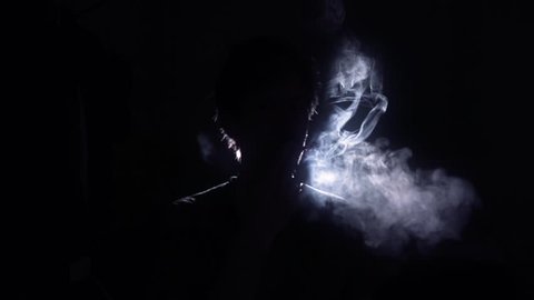 Cigarette smoker silhouette back lit man. Back Lit Silhouette of man smoking in a dark room - 1080p