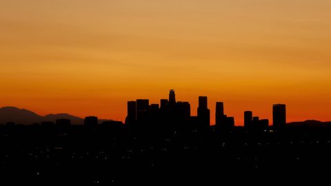 4K Time lapse tilt shot up sunrise over downtown Los Angeles skyline silhouette with red and orange colored sky
