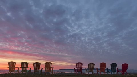 4K Time lapse zoom out of a sunrise behind a row of chairs at lake Huron in Michigan, USA with colored clouds