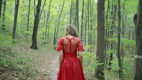 Steadicam shot of a frightened young woman in long red dress run in the woods