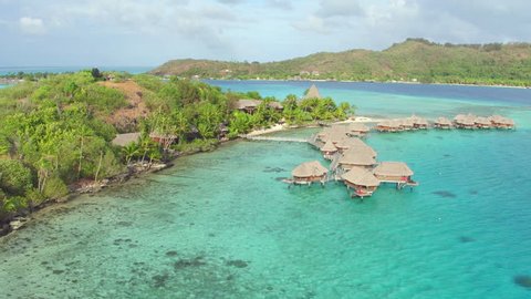AERIAL: Flying around fantastic resort hotel with luxury overwater villas on a small private island with secluded white sand beaches in front of exotic Bora Bora island