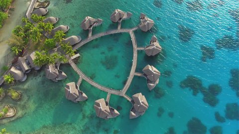 AERIAL: Flying above big luxury overwater bungalow villas along the jetty facing turquoise blue ocean lagoon and tropical white sandy beaches on sunny famous Bora Bora island in French Polynesia