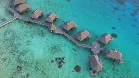 AERIAL: Flying above luxury secluded overwater beachfront villas with perfect exotic ocean view on beautiful tropical island with sandy coastline and palm trees, perfect for dreamy romantic honeymoon