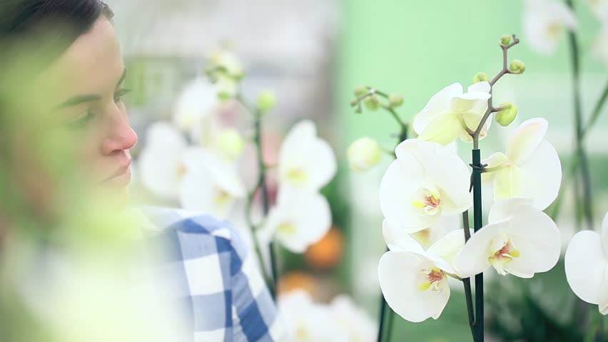 smiling woman in garden of flowers, touches and smells an orchid