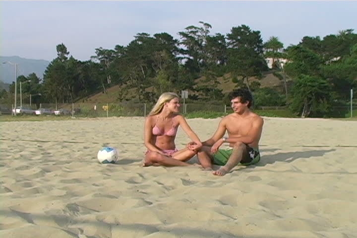 A young man and woman talking on the beach.